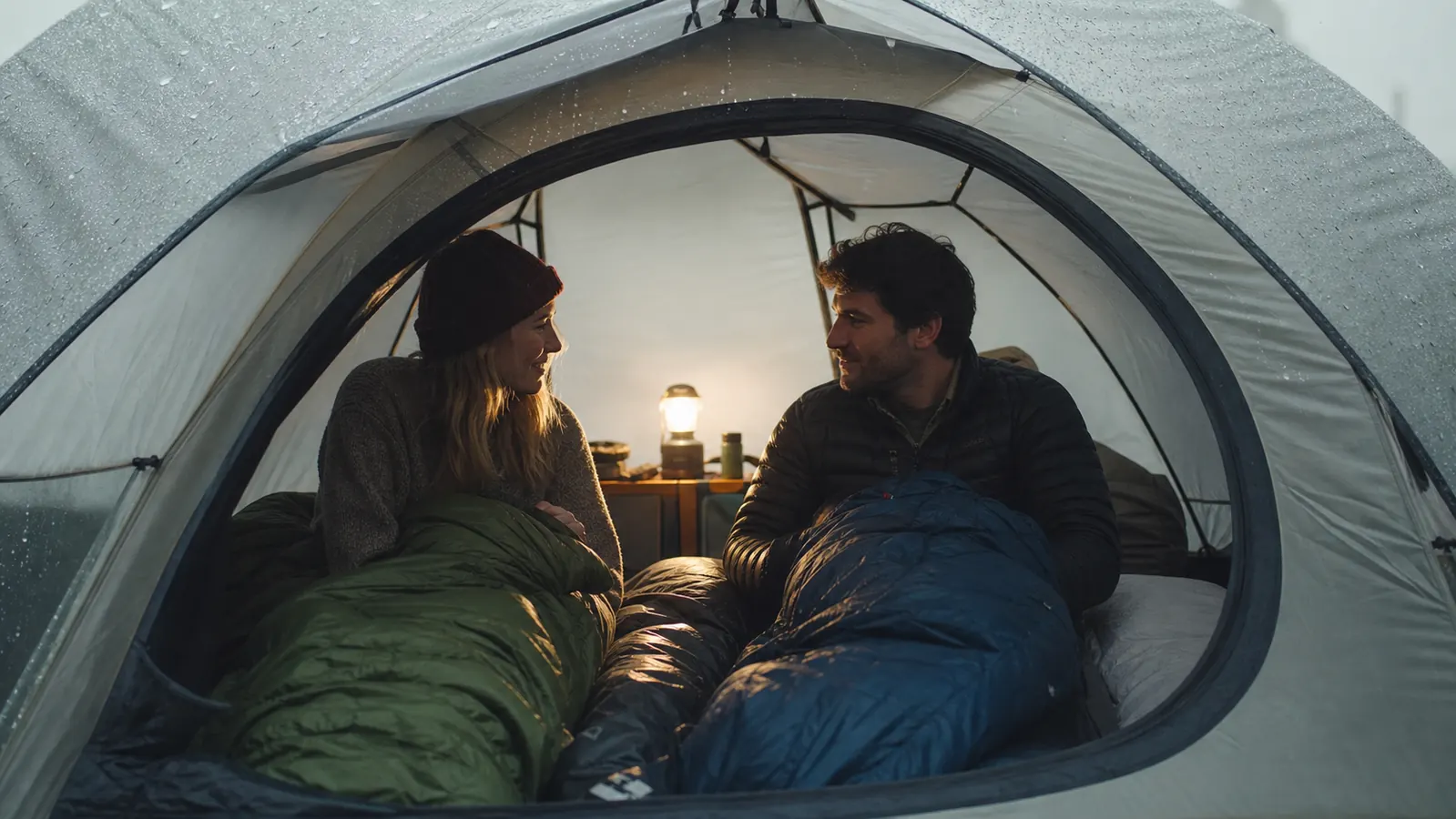 Two campers sitting inside a spacious dome tent during a rain shower, dry and comfortable