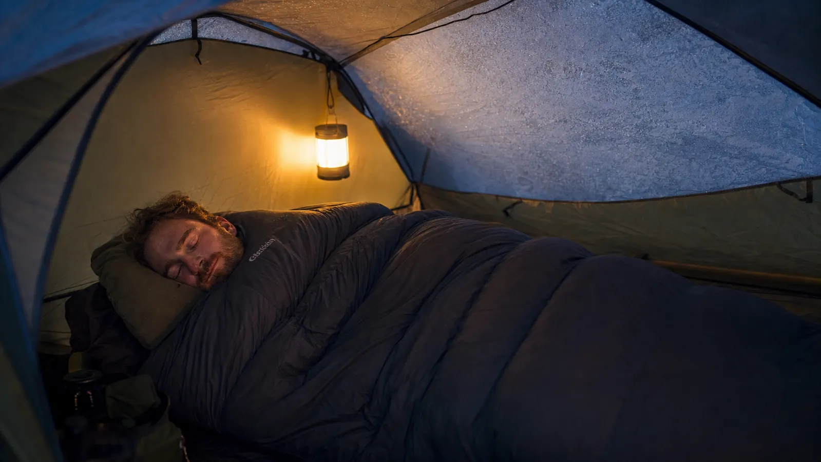Camper sleeping comfortably in a sleeping bag on a pad inside a tent, night shot with soft warm light