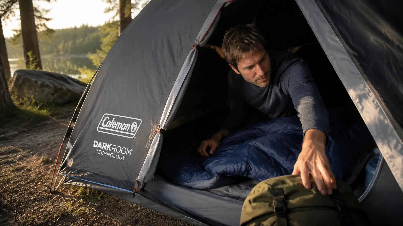 Camper reaching through the single tent door over a sleeping companion to grab gear from the far side of the tent interior