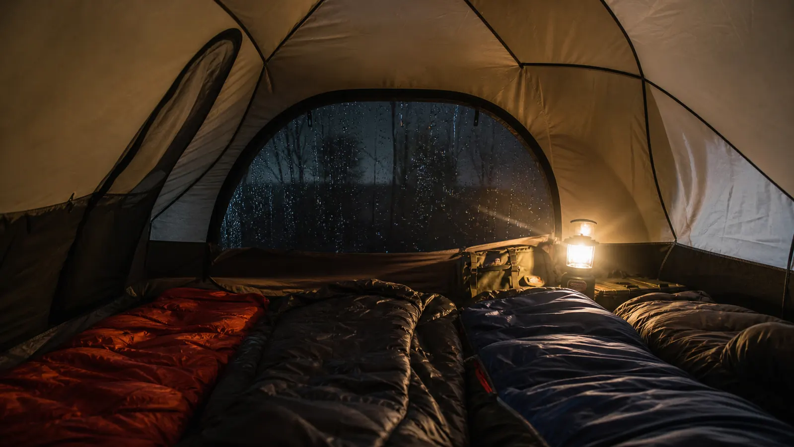 Interior of a dome tent with four sleeping bags arranged inside, raindrops visible on the outer fly