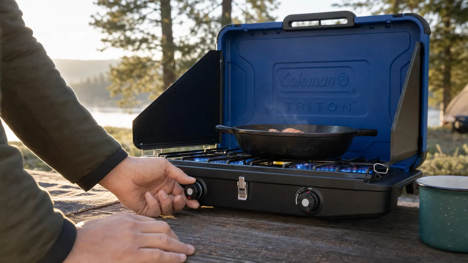 Hand turning the burner knob on a Coleman Triton stove outdoors, propane canister visible in the background