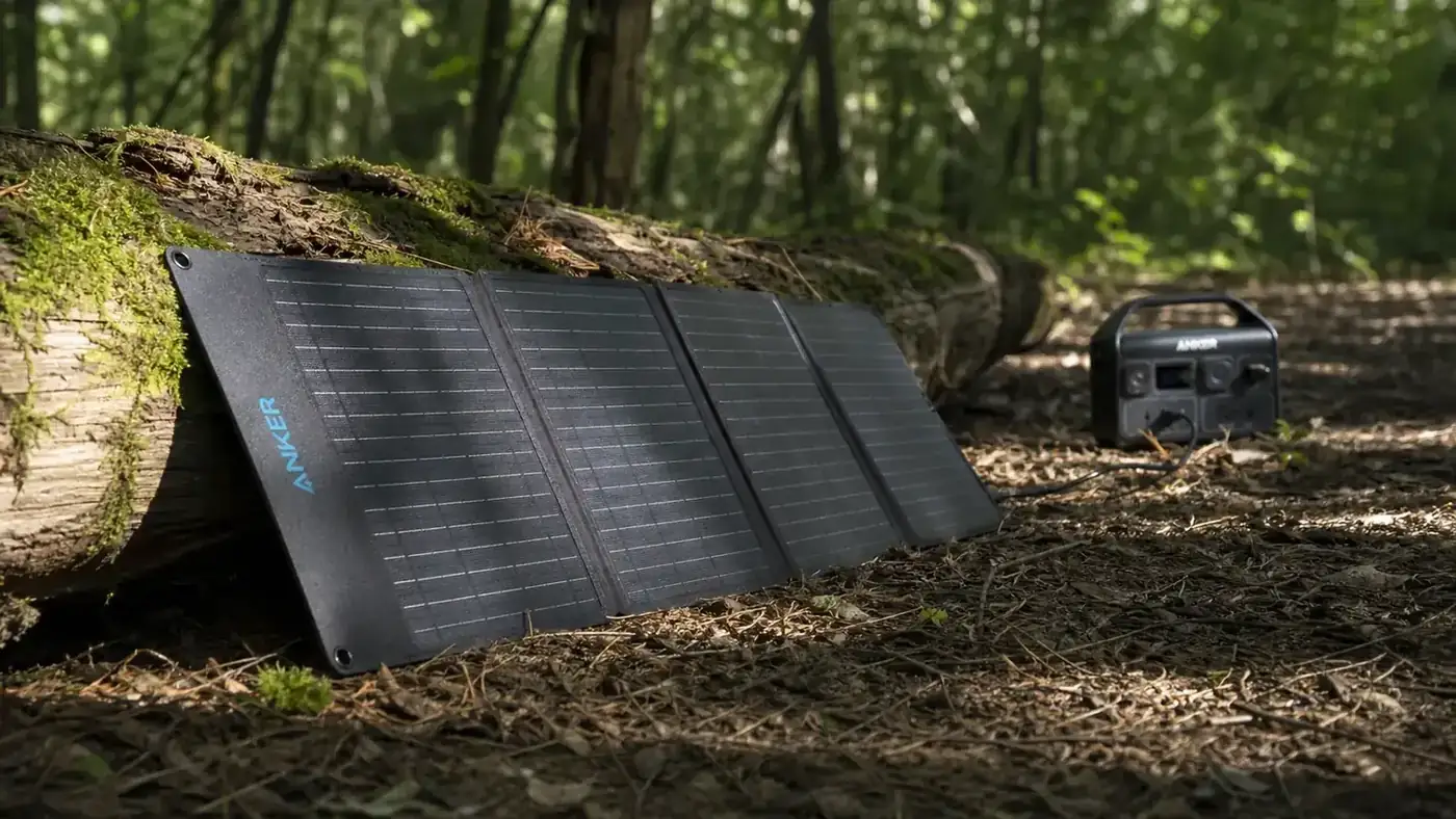 Solar panel propped against a log in a sunny clearing connected by a cable to a portable power station on a folding camp chair